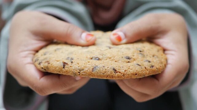 Close up of hands breaking a large chocolate chip cookie in half showing texture and filling