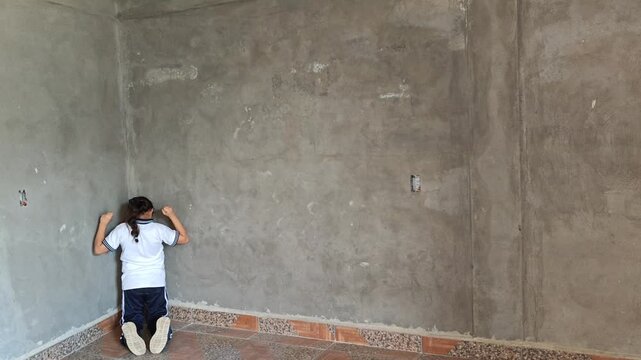 Little girl kneeling in the corner of a wall