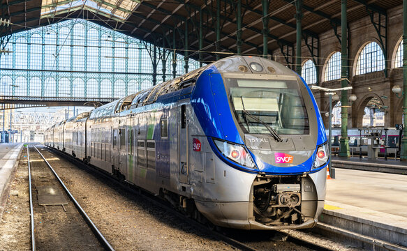 Paris, France - December 16, 2025: Scenic view of a modern SNCF Regio 2N commuter train waiting at the platform under the historic iron and glass roof of the Gare du Nord train station.