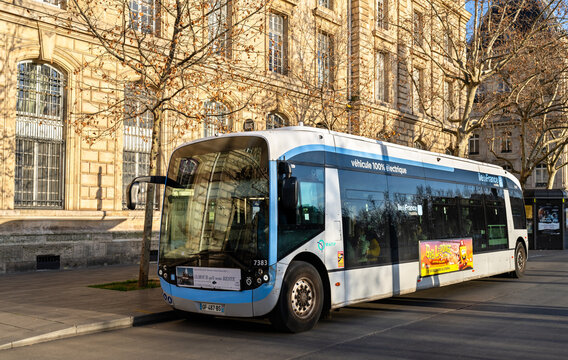 Paris, France - December 16, 2025: Scenic sunny view of a modern electric Alstom Aptis RATP city bus parked in front of the historic stone architecture of the Caserne Verines at Place de la Republique
