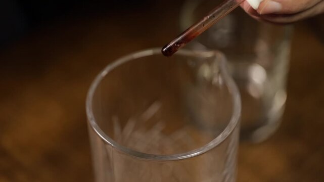 Bartender adding bitters to a mixing glass to prepare an old fashioned cocktail. Old fashioned drink.