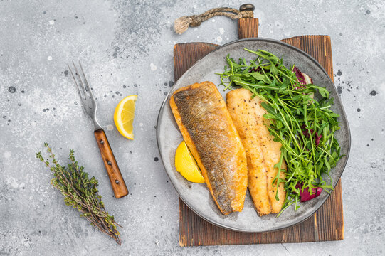 Crispy golden white fish zander fillet with herbs and lemon on plate, healthy seafood meal styled in modern overhead composition.