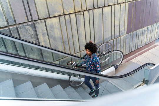 Stylish man carrying bicycle on escalator