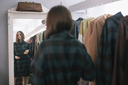Young woman trying dress while looking in mirror at design studio