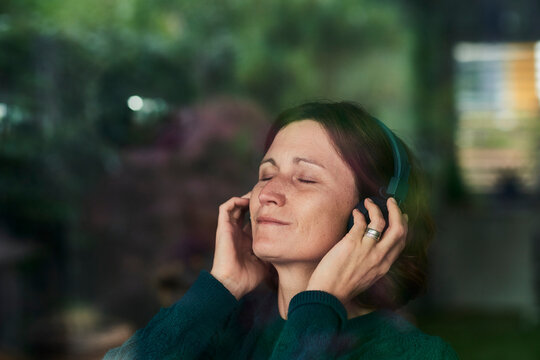 Close-up of woman with eyes closed enjoying music listening through headphones at home