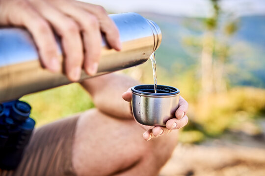 Close-up of man during hiking trip pouring cold water from thermos flask
