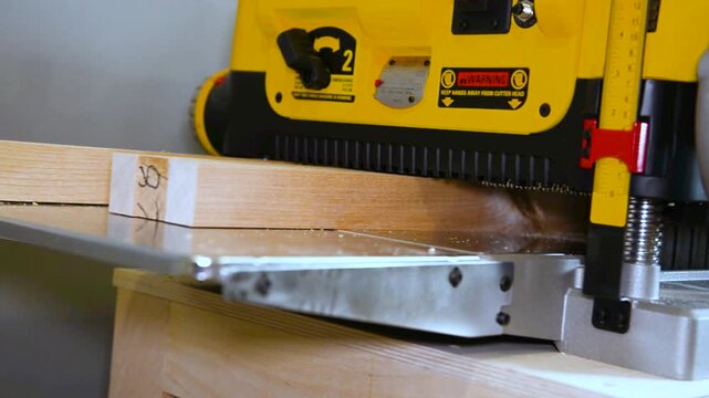 A wood plate passing through the thickness planer machine in a carpentry workshop. Woodworking process, furniture preparation, handmade craftsmanship, carpentry studio.