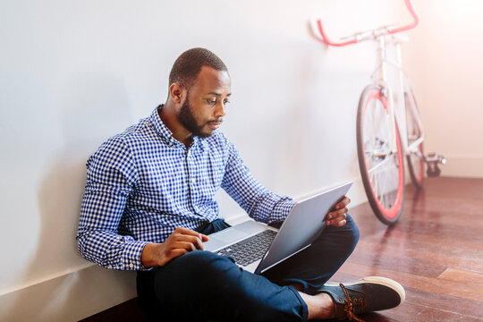 Man using laptop sitting on wooden floor with bicycle in background