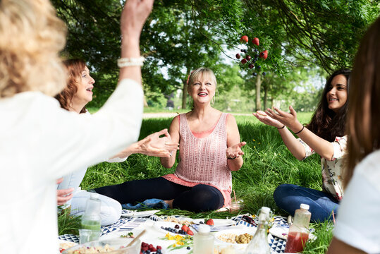 Happy women throwing berries in the air at a picnic in park