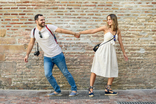 Happy couple holding hands walking in opposite directions at brick wall