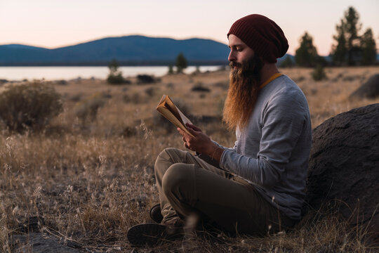 USA, North California, bearded young man reading a book near Lassen Volcanic National Park