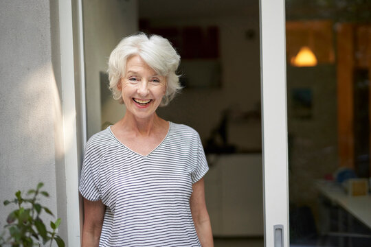 Portrait of laughing mature woman standing in front of opened terrace door in the evening