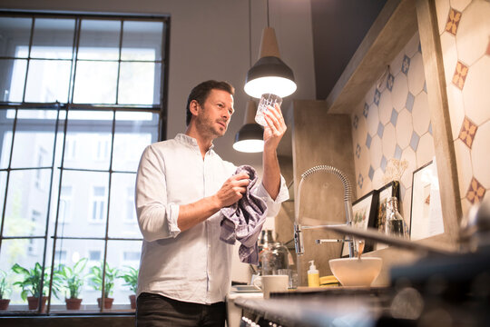 Man in kitchen drying glass with towel