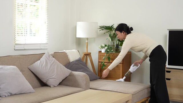 Woman Cleaning Sofa With Vacuum Cleaner At Home. vacuuming sofa in bright living room enjoying housework and domestic chores
