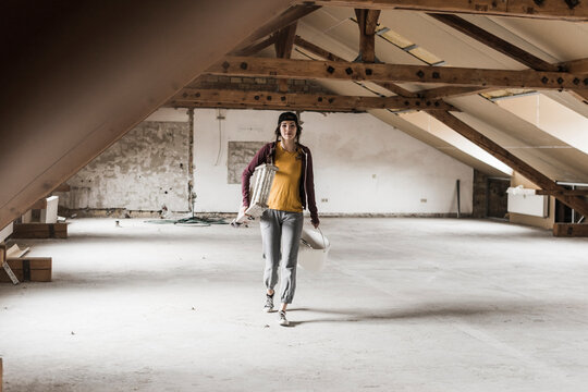 Young woman on construction site carrying ladder and paint bucket
