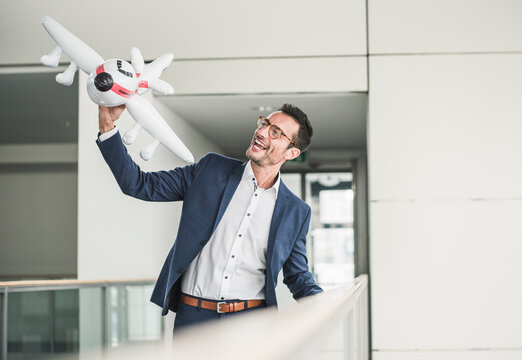 Laughing businessman playing with toy aeroplane in office building