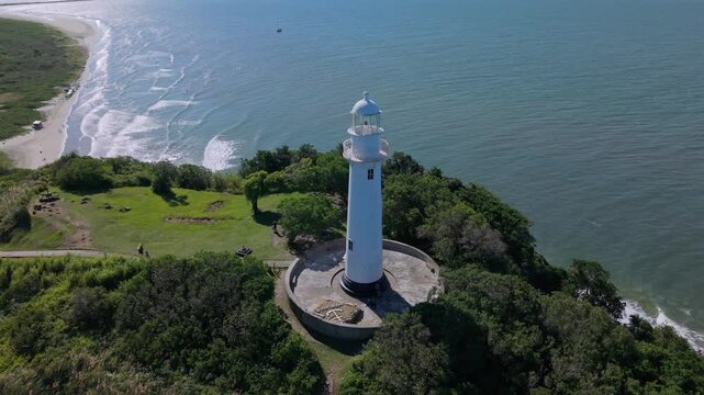 Aerial establishing orbit of lighthouse on green headland above ocean, , Lighthouse of the Shells or Faro de las Conchas, Brazil