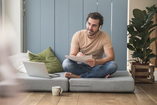 Young mamn sitting on mattress, taking notes, using headphones