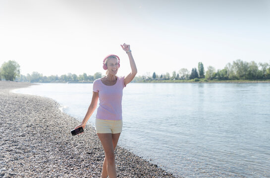 Happy mature woman listening to music with headphones at the riverside