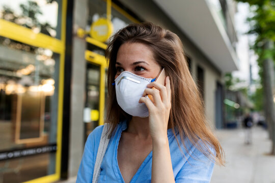 Close-up of young woman wearing mask talking over smart phone in city
