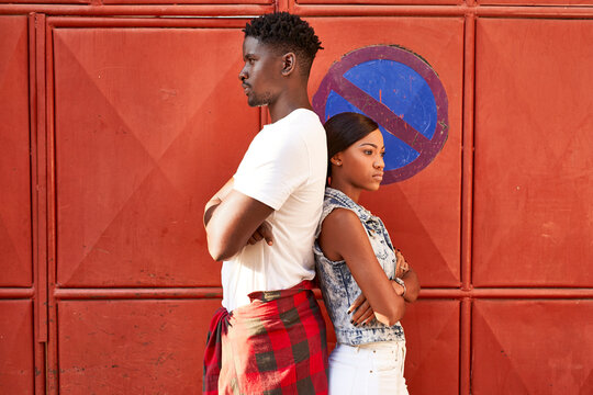 Sulking couple standing back to back in front of red gate