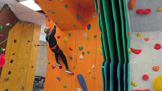 A teenager climbs the overhanging wall of a climbing wall indoors - strength, technique and concentration training with insurance.
