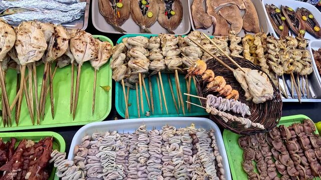 Candid handheld overhead view of an assortment of authentic Filipino street food inihaw or skewers while hands are picking and choosing what to buy. Kabankalan, Negros Occidental, Philippines