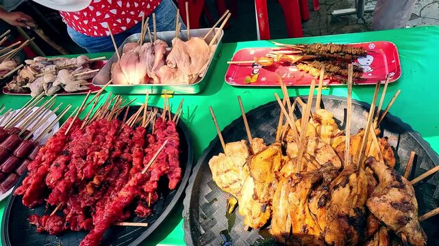 Candid handheld motion dolly forward showing an assortment of grilled meat skewers displayed at a vibrant street food market featuring authentic traditional local Filipino cuisine