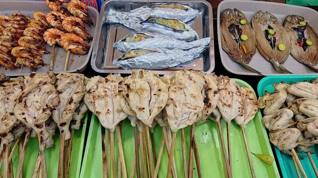 Overhead handheld motion showing hands arranging assorted grilled seafood and chicken skewers on trays at a hawker food stall. Traditional authentic local Filipino cuisine