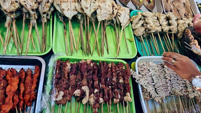 A variety of grilled meat skewers displayed on colorful trays at a street food stall showing the authentic local Filipino street food like isaw, bangus and liver. Kabankalan, Philippines