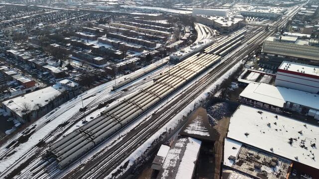 High angle drone view of passenger trains parked at a railway depot and shunting yard surrounded by a snow covered urban industrial landscape during a sunny winter day