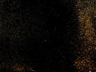 Obraz premium Abstract gold glitter particles sparkling on a black background. Luxury shiny black texture with glowing golden dust wave.
