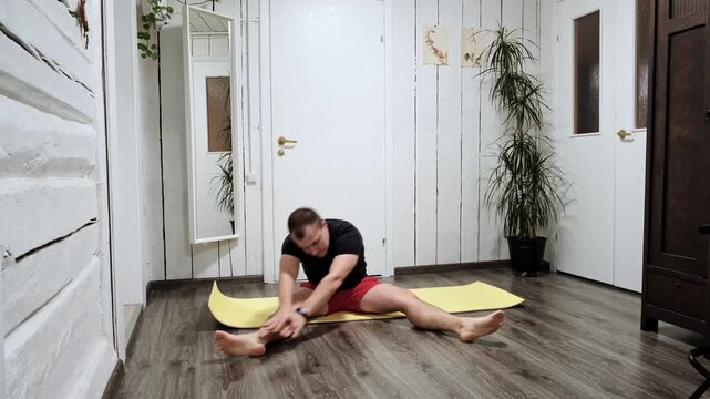 The man doing a seated forward bend stretch to limber up his hamstrings before starting home. Person practicing flexibility. Healthy lifestyle concept. Stretching exercise. High quality 4k footage.