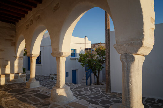 Traditional white Greek buildings viewed through old stone arches in Paroikia (Parikia) town on Paros island in Greece at sunset.