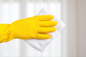 Cleaning cloth with yellow rubber glove hand wiping surface in bright room, minimal style close up realistic editorial photograph