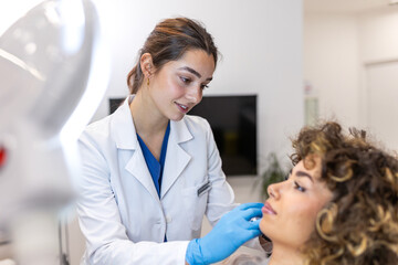 Professional dermatologist examining young woman's face in aesthetic clinic. Female doctor in white...