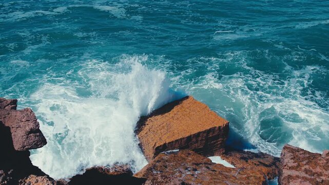 Slow motion video: Crashing waves creating huge splashes.  Ocean Waves at high tide roll in and crash against the coastal cliffs, huge rocks while summer sunny day.