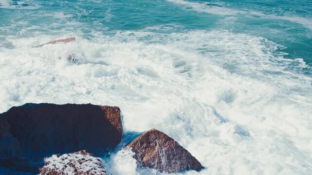 Waves at high tide roll in and crash against the coastal cliffs, huge rocks. Close-up of crashing ocean waves creating huge splashes.