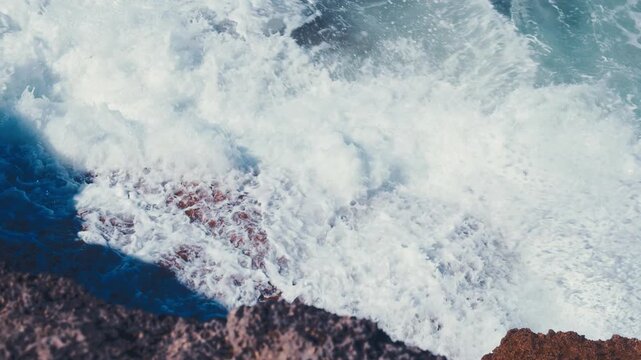 Slow motion video: Crashing waves creating huge splashes.  Ocean Waves at high tide roll in and crash against the coastal cliffs, huge rocks while summer sunny day.