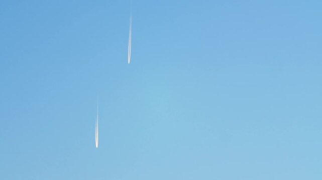 Two passenger planes are flying high in the sky, leaving a long white plume of fuel. Flying aircrafts high in the sky leaving a white trail.