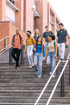 Diverse group of young students walking down urban university stairs together, enjoying college life and education