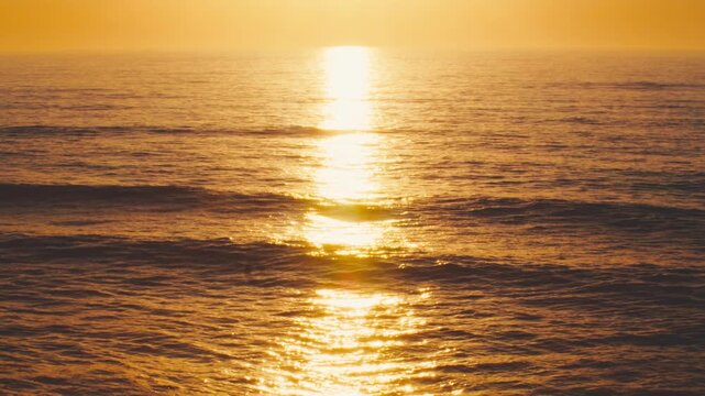 An orange sunset with a large and bright sun above the horizon of the ocean water surface. A picturesque sunrise over the sea, painted in a bright orange color. A soothing sunset scene over the ocean.