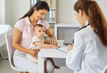 Fototapeta premium Mother and baby meet pediatrician for checkup. In medical clinic, family doctor notes and discusses growth, vaccines, and development with mother. Concept child health, care, medicine and support.