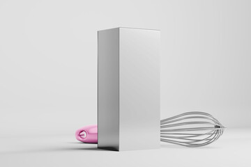 A tall, rectangular object stands upright with a pink-handled whisk partially hidden behind it and a metal whisk lying on the surface to the right © cozzdesign