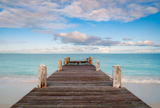 Looking down wooden pier on beach into the Caribbean ocean.