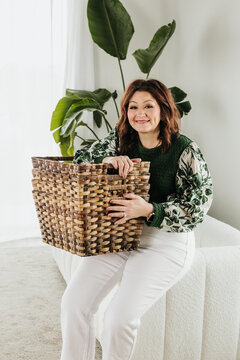 Woman sitting on edge of white couch holds stack of baskets