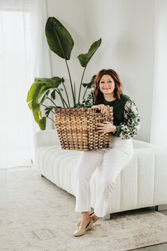 Woman sitting on edge of white couch holds stack of baskets