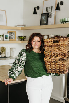Woman holds stack of four wicker baskets while standing in kitchen