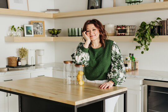 Woman leans elbow on glass jar full of lemons while in kitchen