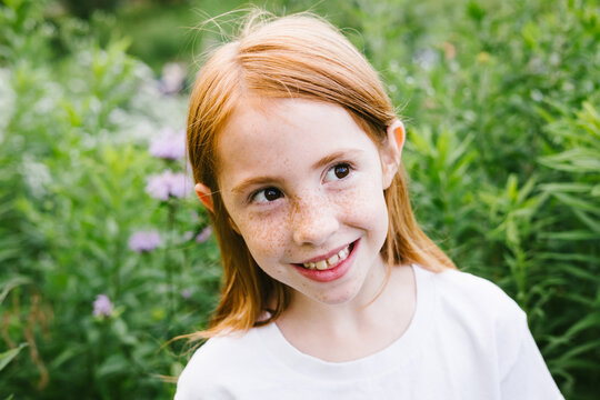 Happy red hair girl with freckles outside by field of purple flowers